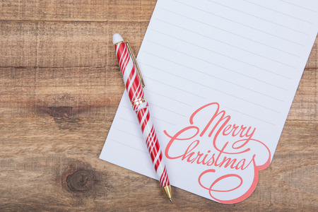 Winter Holidays decoration with white Merry Christmas note and red and white striped pen on wooden background.の写真素材