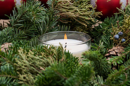 Winter holiday decoration: fraser fir table wreath centerpiece with cones, juniper, Christmas tree balls and burning white candle.の写真素材