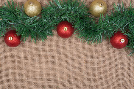 Winter holiday decoration: green garland and Christmas tree balls on burlap backgroundの写真素材
