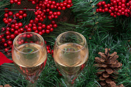 Winter holiday decoration: blooming holiday red poinsettia, pine, berry bush, cones and two glasses of white wine.の写真素材