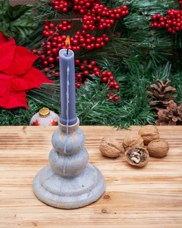 Winter holiday decoration: Blooming Red Poinsettia, Pine, Berry bush, Christmas tree balls, walnut and burning blue candle on wooden background.の写真素材