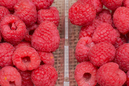 Macro shot of ripe organic raspberries in plastic box on burlap background