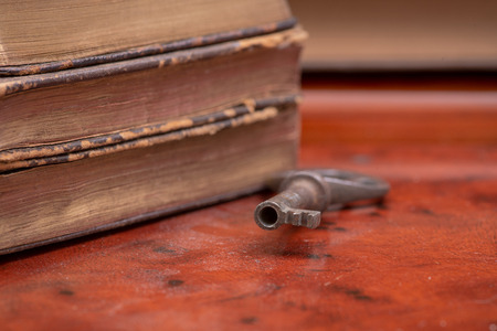 Pile of old vintage hard cover books and antique metallic key on wooden backgroundの写真素材