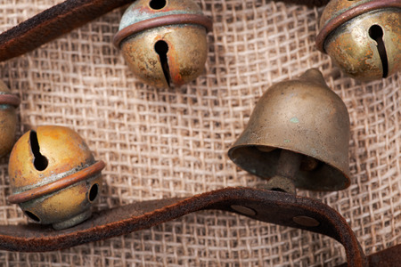 Antique vintage oxidize brass sleigh bells on leather strap and burlap backgroundの写真素材