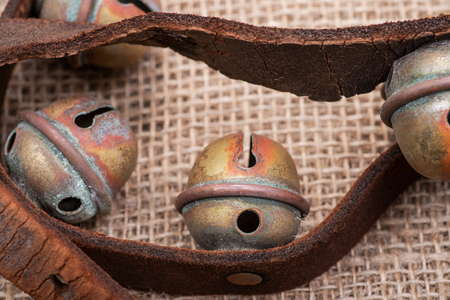 Antique vintage oxidize brass sleigh bells on leather strap and burlap backgroundの写真素材