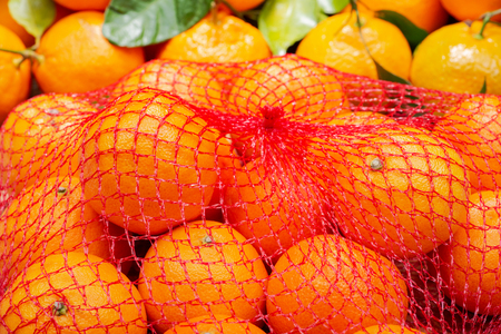 Fresh ripe organic mandarins in plastic mesh sack on olive wood and burlap background.の写真素材