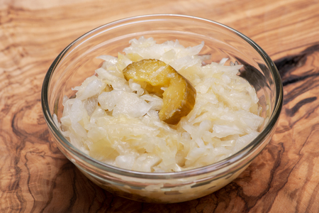 Traditional organic raw and fermented sauerkraut with pickled Persian cucumbers in clear glass bowl on cork backgroundの写真素材