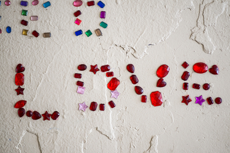 LOVE word glued to a concrete white wall outdoors using colorful glass gems and beads.の写真素材