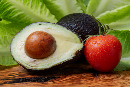 Fresh Organic Avocado cut in half and Organic Red Tomatoes on the vine arranged on natural olive wood.の写真素材