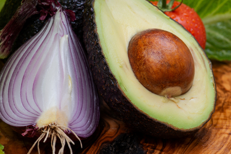 Organic Fresh Avocado cut in half, Red Onions and Red Tomatoes on the vine arranged on natural olive...
