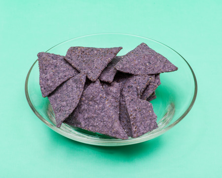 Lightly Salted Organic Blue Corn Tortilla Chips in clear glass bowl isolated on green background.