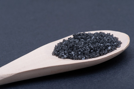 Hawaiian Black Lava Sea Salt in handmade wooden spoon on dark background.