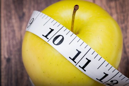 Yellow Apple and Soft Vinyl Measuring Tape on wooden background.