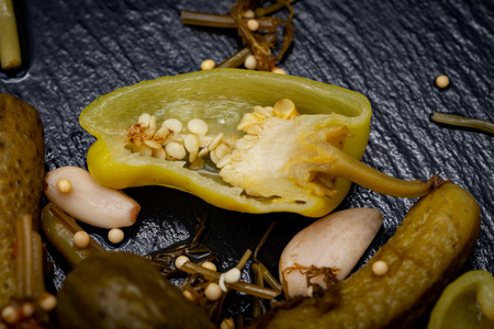 Cornichons (Mini French style Gherkin Cucumbers) and Pickled Pepperoncini Peppers on natural stone background.の写真素材