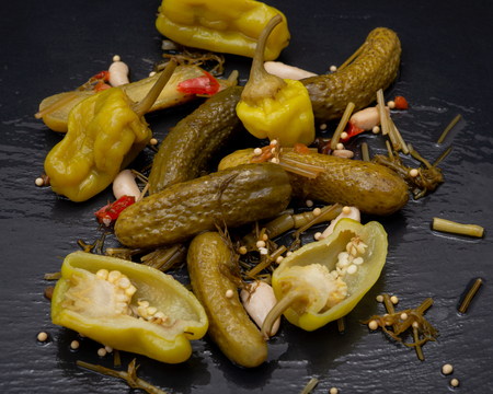 Cornichons (Mini French style Gherkin Cucumbers) and Pickled Pepperoncini Peppers on natural stone background.の写真素材