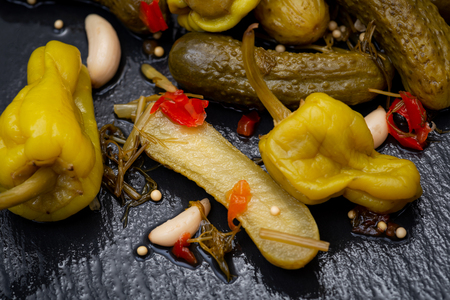 Cornichons (Mini French style Gherkin Cucumbers) and Pickled Pepperoncini Peppers on natural stone background.の写真素材