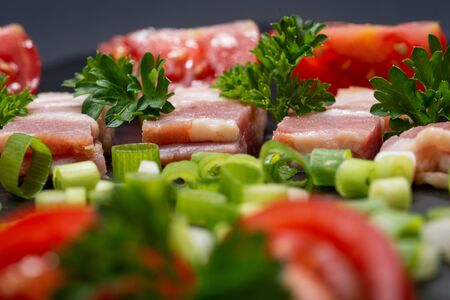 Uncured Apple Smoked Bacon, Red Tomatoes, fresh Curly Parsley and Green Onion Scallions arranged on natural black stone background.の写真素材