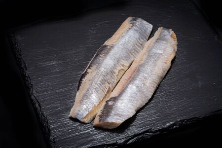 Salted boneless fillets of wild-caught Atlantic Herring arranged on natural black stone background. Clupea harengus.の写真素材