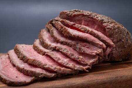 Sliced Grass Fed juicy Corn Roast Beef on natural wood cutting board.