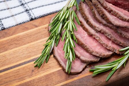 Sliced Grass Fed juicy Corn Roast Beef garnished with Rosemary Fresh Herb on natural wood cutting board.の写真素材