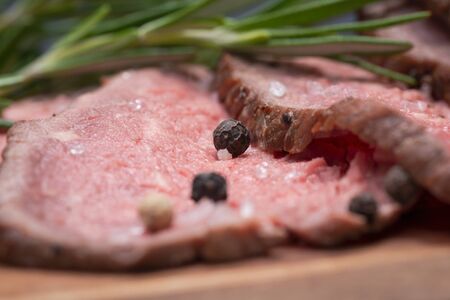 Sliced Grass Fed juicy Corn Roast Beef garnished with Fresh Rosemary Herb and Rainbow Peppercorns on...