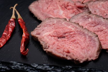 Sliced Grass Fed Juicy Corn Roast Beef garnished with dried Red Chile De Arbol Pepper on black...