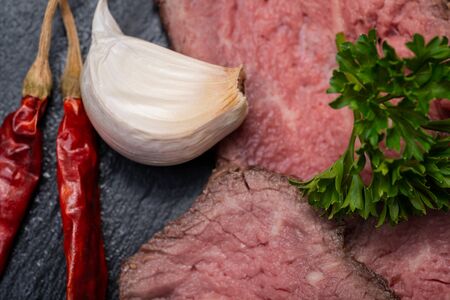 Sliced Grass Fed Corn Roast Beef garnished with Garlic, Fresh Curly Parsley and dried Red Chile De...