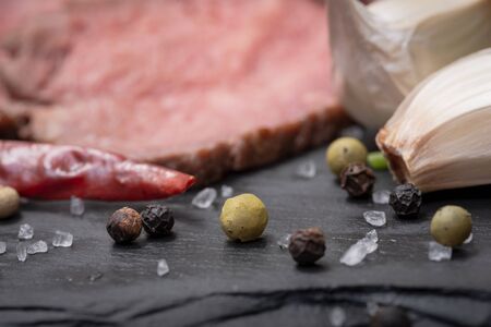 Grass Fed Corn Roast Beef garnished with Fresh Parsley, dried Red Chile Pepper, Garlic and Rainbow  Peppercorns on natural black stone background.の写真素材