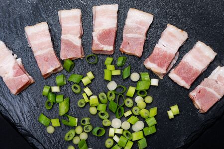 Uncured Apple Smoked Bacon garnished with Green Onion Scallions. Black natural stone background.の写真素材