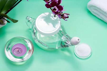 Neti Pot, pile of Saline, rolled White Towels, Purple Orchid Flowers and Lavender Tea Light Candle on green background. Sinus wash. Nasal irrigation.の写真素材