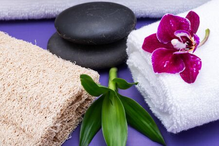 Spa Wellness Concept. Natural Loofah Sponge, rolled up White Towels, stacked Basalt Stones, Bamboo...