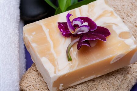 Spa Wellness Concept. Natural Loofah Sponge, Almond Goat's milk Soap, White Towels, Basalt Stones, Bamboo and Orchid Flower on purple background.の写真素材