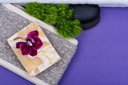 Spa Wellness Concept. Natural Cotton & Flaxseed Back Scrubber, Almond Goat milk Soap, Basalt Stones, Orchid and Dianthus Flowers on purple background.の写真素材