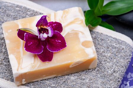 Spa Wellness Concept. Natural Cotton & Flaxseed Back Scrubber, Almond Goat milk Soap, Basalt Stones, Orchid and Dianthus Flowers on purple background.の写真素材