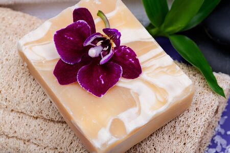 Spa Wellness Concept. Natural Loofah Sponge, Almond Goat's milk Soap, White Towels, Basalt Stones, Bamboo and Orchid Flower on purple background.の写真素材