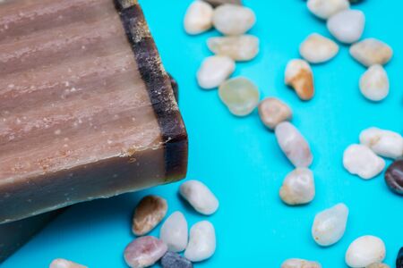 Handmade ultra-moisturizing Frankincense and Myrrh  Scented Goat's Milk Bar Soap decorated with small stone Pebbles on bright blue background.の写真素材