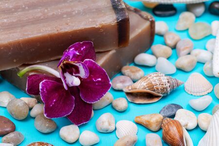 Handmade moisturizing Frankincense & Myrrh Goat's Milk Bar Soap decorated with Pebbles, Sea Stars, Sea Shells and Orchid Flower on blue background.の写真素材