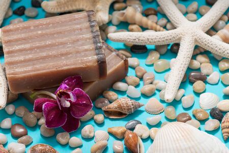 Handmade moisturizing Frankincense & Myrrh Goat's Milk Bar Soap decorated with Pebbles, Sea Stars, Sea Shells and Orchid Flower on blue background.の写真素材