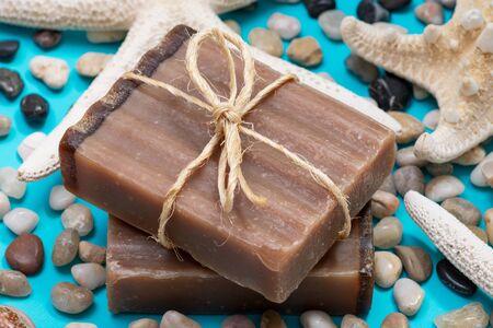 Handmade moisturizing Frankincense & Myrrh Goat's Milk Bar Soap decorated with small Pebbles, Sea Stars and Sea Shells on bright blue background.の写真素材