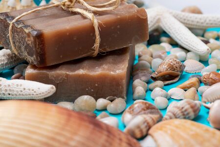 Handmade moisturizing Frankincense & Myrrh Goat's Milk Bar Soap decorated with small Pebbles, Sea Stars and Sea Shells on bright blue background.の写真素材