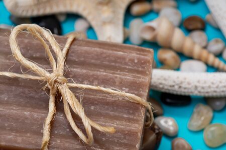 Handmade moisturizing Frankincense & Myrrh Goat's Milk Bar Soap decorated with small Pebbles, Sea Stars and Sea Shells on bright blue background.の写真素材