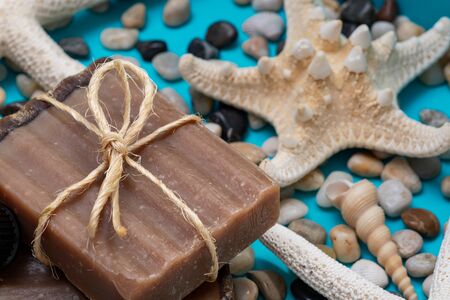 Handmade moisturizing Frankincense & Myrrh Goat's Milk Bar Soap decorated with small Pebbles, Sea Stars and Sea Shells on bright blue background.の写真素材