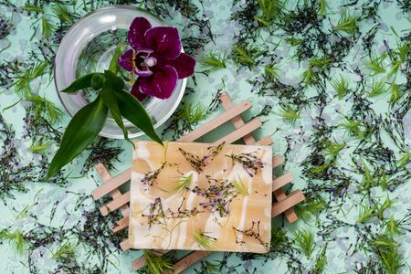 Wooden Soap Holder with Handmade Almond Scented Goat's Milk Bar Soap decorated with Orchid Flower, Bamboo and  flower sprinkles on green background.の写真素材