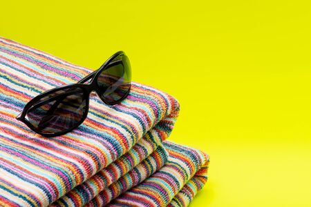 Folded Colorful Striped Organic Cotton Beach Towels and black Sunglasses on bright yellow background as Summer Vacation Theme.の写真素材