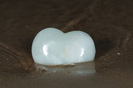 Polished cream white carved Onyx Heart on wet sand on the beach at sunrise in front of the lake. Love, Romance and Friendship concept.の写真素材
