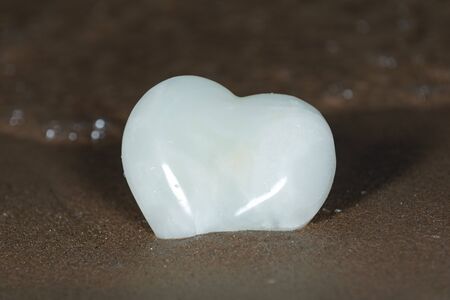 Polished cream white carved Onyx Heart on wet sand on the beach at sunrise in front of the lake. Love, Romance and Friendship concept.の写真素材