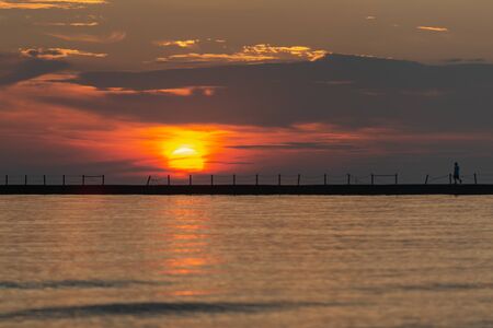 Silhouette of a walking man at a Pier at Sunrise with Sun reflecting in the Lake Michigan.の写真素材