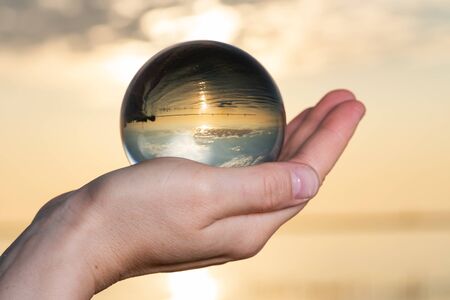 Woman's hand holding high grade Clear Quartz Sphere at the sunrise in front of the lake.
