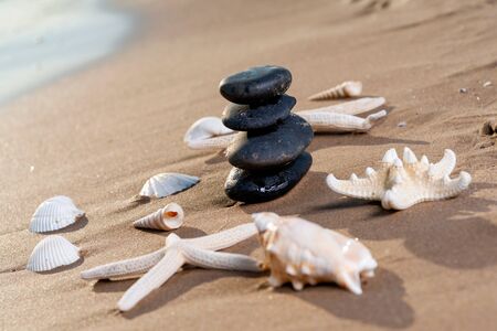 Spa composition - stacked Basalt Stones, Seashells and Sea Stars on the beach at sunrise in front of the ocean. Wellness, Balance and Relax concept.の写真素材