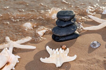 Spa composition - stacked Basalt Stones, Seashells and Sea Stars on the beach at sunrise in front of the ocean. Wellness, Balance and Relax concept.の写真素材